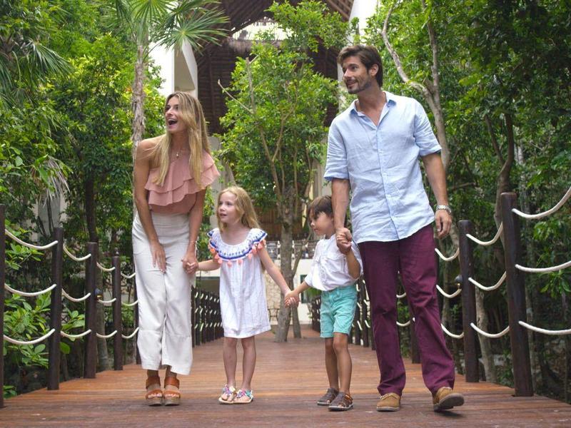 Famiglia con due bambini che cammina su un ponte di legno circondato dal verde.
