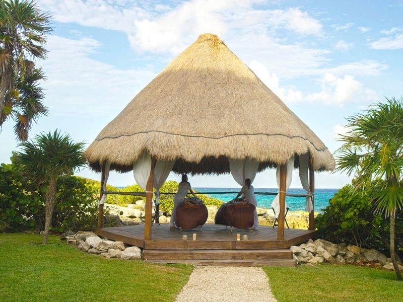 Capanna sulla spiaggia con tetto di paglia circondata da palme e erba verde con vista mare.