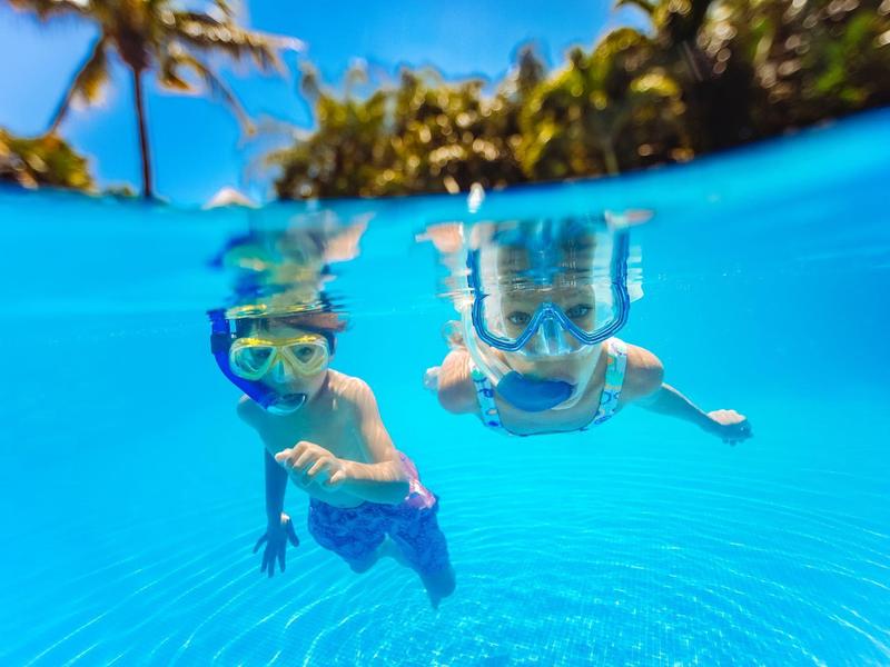 Due bambini fanno snorkeling in acqua blu limpida sotto le palme in una giornata di sole.