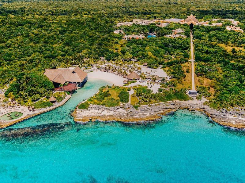 Un resort con un ponte, circondato da una fitta vegetazione e acqua turchese sulla riva.