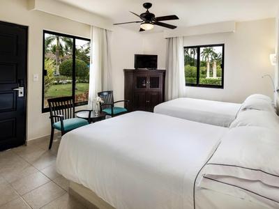 Camera d'hotel con due letti queen, una TV, una sedia e vista sul giardino