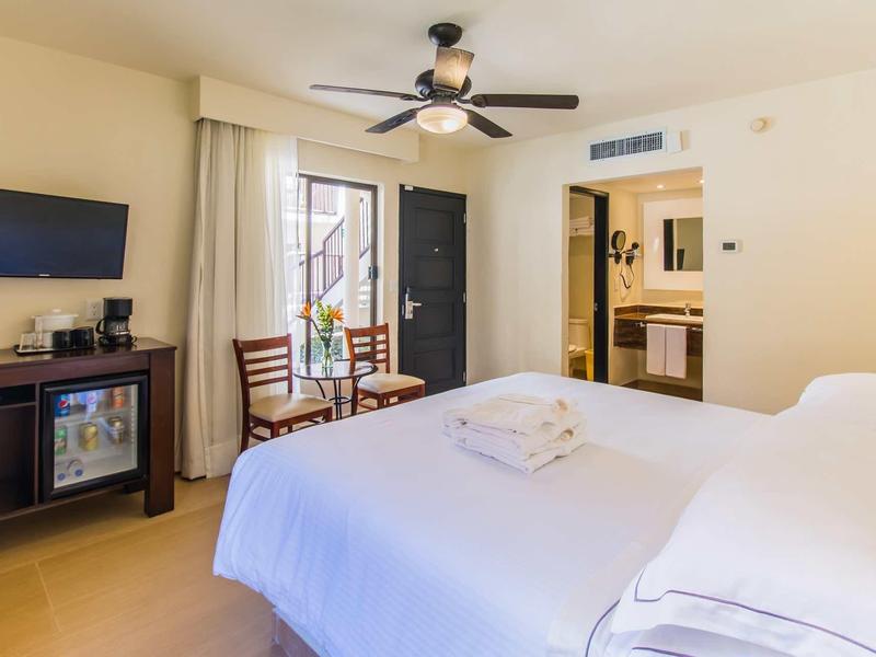 Camera d'hotel luminosa con letto grande, ventilatore a soffitto e accesso al balcone.