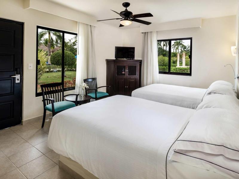 Camera d'hotel con due letti queen, una TV, una sedia e vista sul giardino