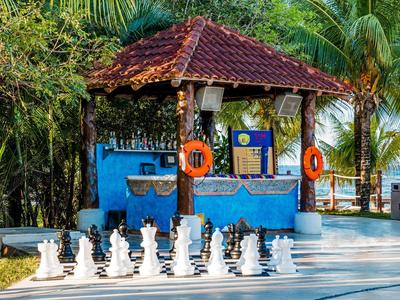 Großes Schachspiel im Freien vor blauem Kiosk mit roten Rettungsringen und Palmen im Hintergrund.