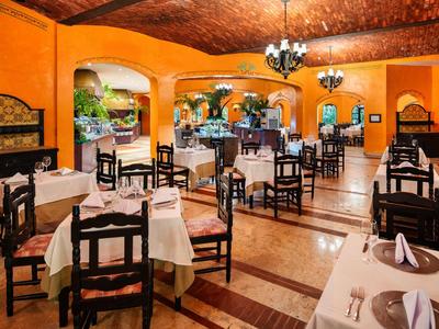 Weitläufiges Restaurant mit orangen Wänden, dunklen Holztischen und weißen Tischdecken.