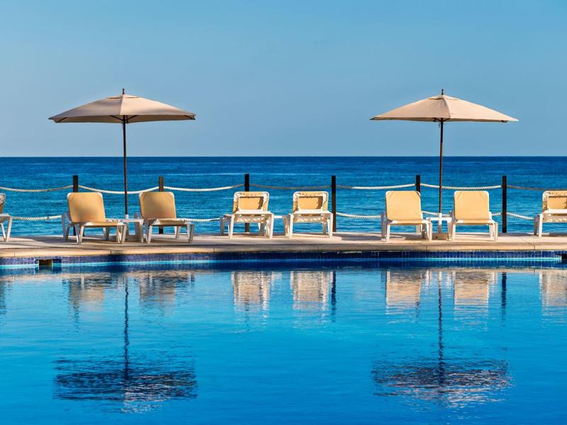 Piscina blu chiara con lettini e ombrelloni vicino al mare.