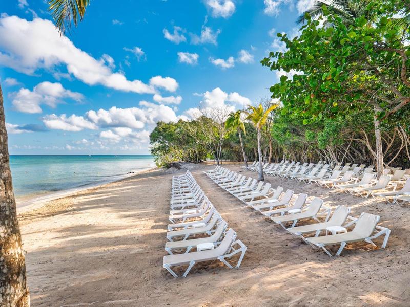 Fila di sedie a sdraio bianche su spiaggia sabbiosa sotto cielo azzurro con alcune nuvole.