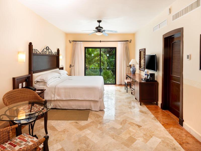 Camera d'hotel luminosa con letto grande, TV a schermo piatto e vista su un giardino verde.