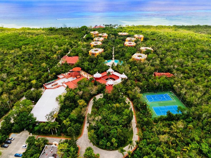 Complesso di lusso con tetti rossi circondato da fitta vegetazione e campo da tennis vicino al mare