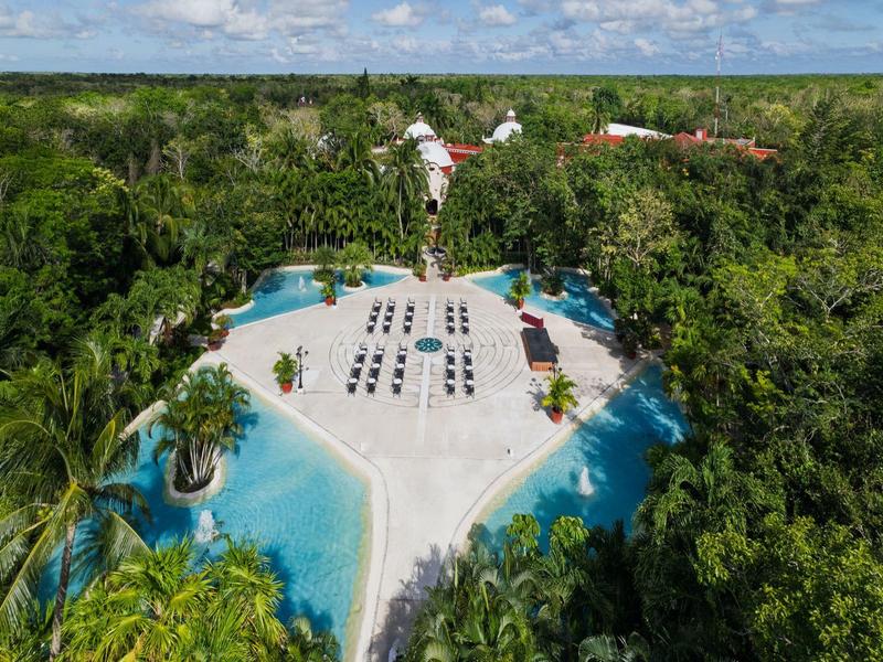 Area piscina di un resort con lettini circondata da vegetazione tropicale sotto un cielo azzurro.