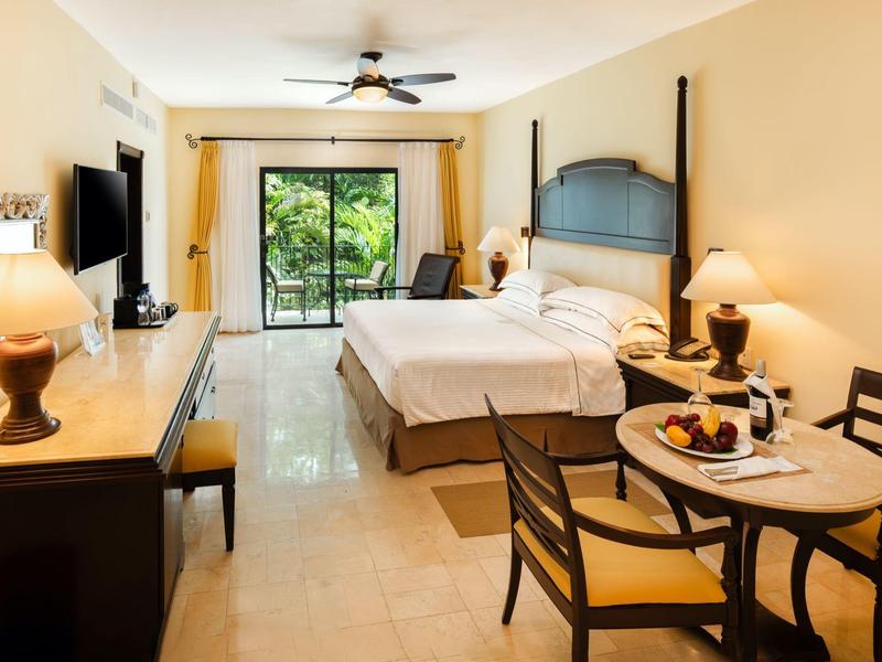 Camera d'hotel luminosa con letto matrimoniale, scrivania, tavolo con sedie e vista sul balcone.