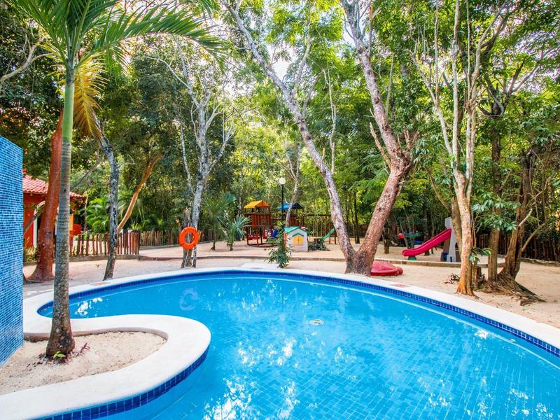 Piscina curva con acqua azzurra chiara circondata da alberi e sdraio all'aperto.