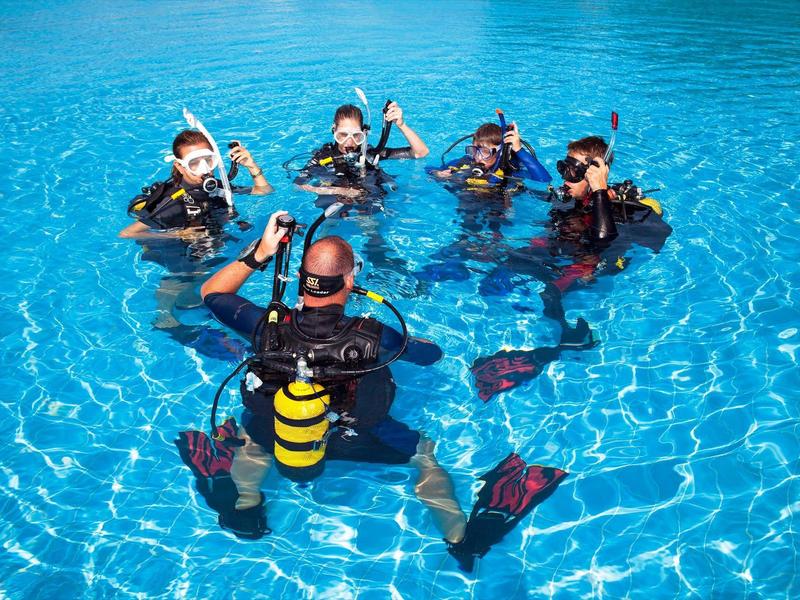 Cinq plongeurs en équipement complet dans une piscine bleue claire, formant un cercle.