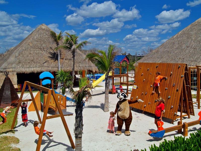 Enfants jouant dans un parc avec balançoires et murs d'escalade sous des huttes.