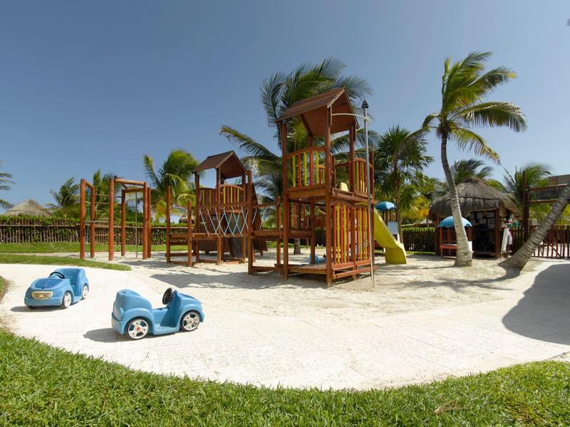 Aire de jeux en bois avec voitures bleues pour enfants sous un ciel clair.