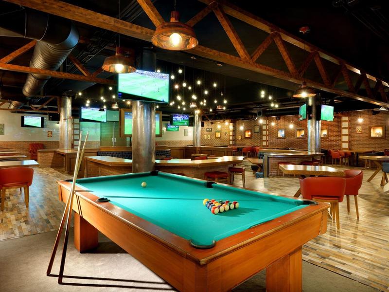 Salle de billard lumineuse avec table verte et tabourets rouges dans un lieu de détente.