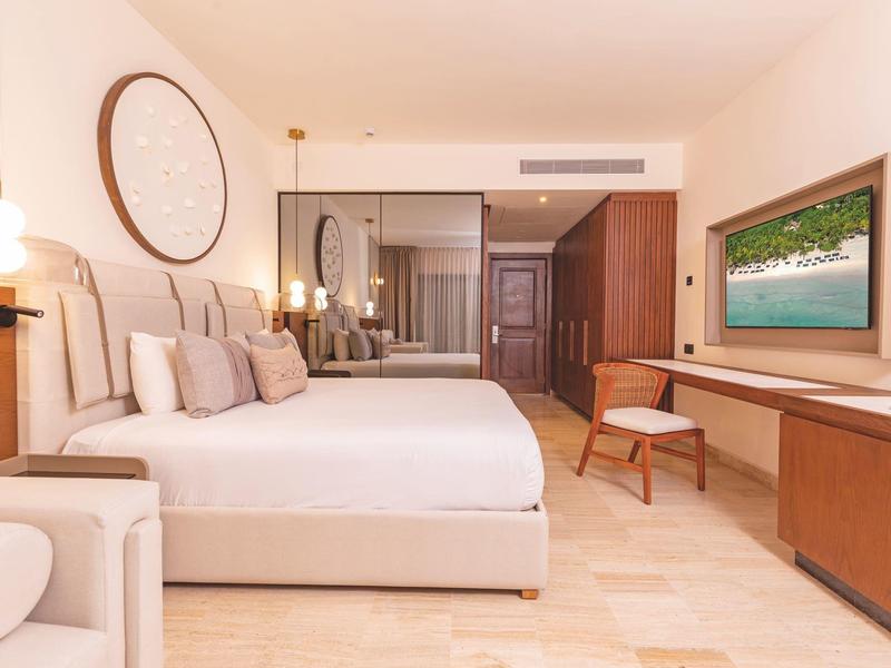 Chambre d'hôtel moderne avec grand lit blanc, décoration minimaliste et télévision murale.