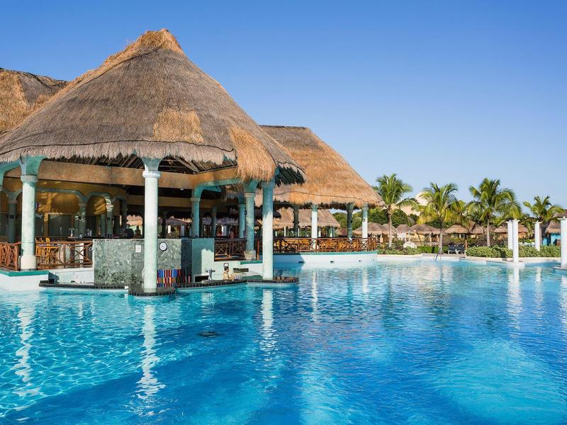 Bar dans une piscine avec toit de chaume sous un ciel bleu clair.
