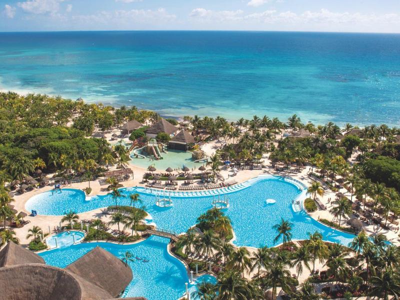 Vue aérienne d'une station balnéaire avec piscines et plage entourée de végétation.