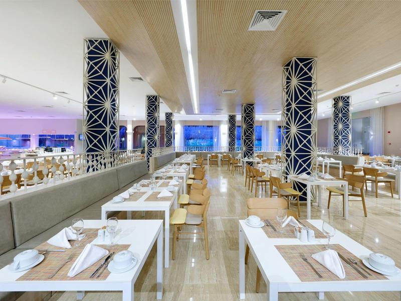 Salle à manger d'hôtel moderne avec tables blanches et sièges en bois clair.