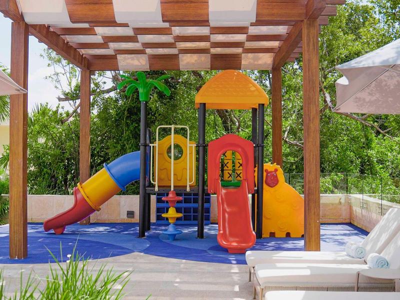 Aire de jeux colorée sous pergola avec toboggans, entourée de chaises longues.
