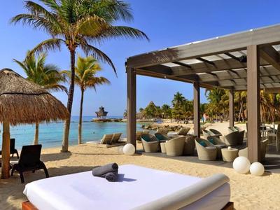 Strand met loungegedeelte, palmbomen en rieten dak, zee en boten op de achtergrond.