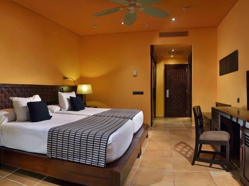 Modern hotelkamer met tweepersoonsbed, bureau en tv in warme kleuren.