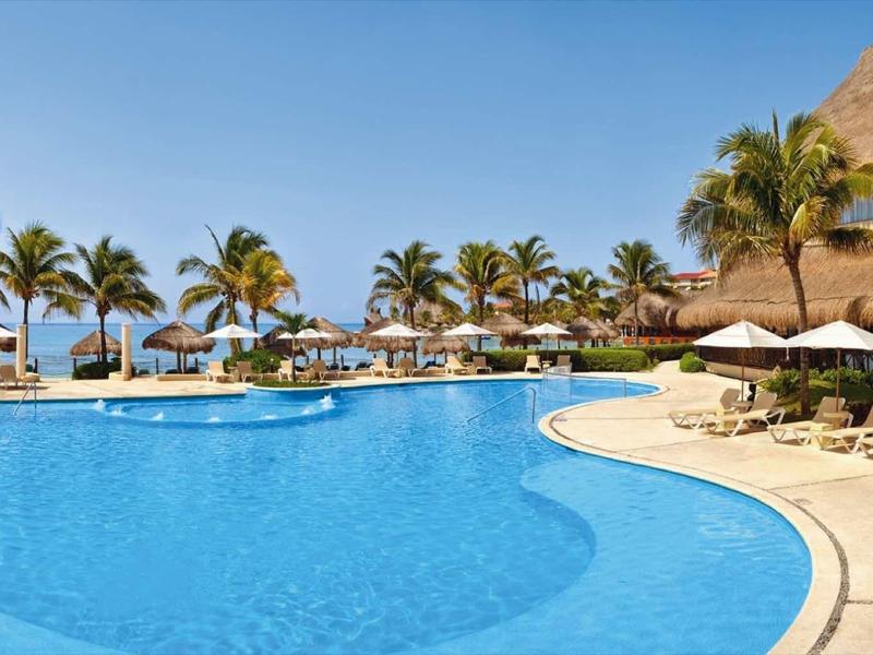 Groot buitenzwembad met ligstoelen en palmbomen in een tropisch resort bij heldere lucht.