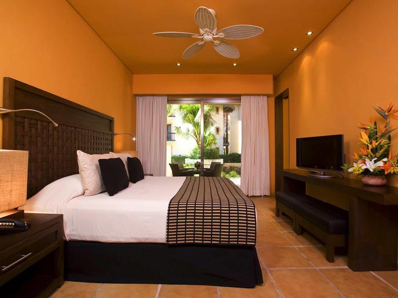 Gezellige hotelkamer met groot bed, plafondventilator en balkon met uitzicht op de tuin.