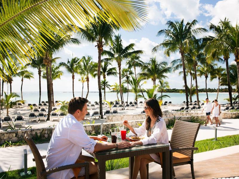 Coppia seduta all'aperto sotto palme, gustando bevande con vista mare.