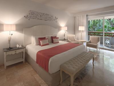 Helles Schlafzimmer mit großem Bett, roten Akzenten, Nachttischen, Lampen und Balkon mit Waldsicht.