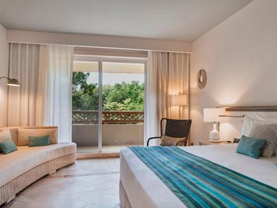 Helles Schlafzimmer mit großem Bett, blauem Läufer, Sofa, Fenster mit Blick ins Grüne.