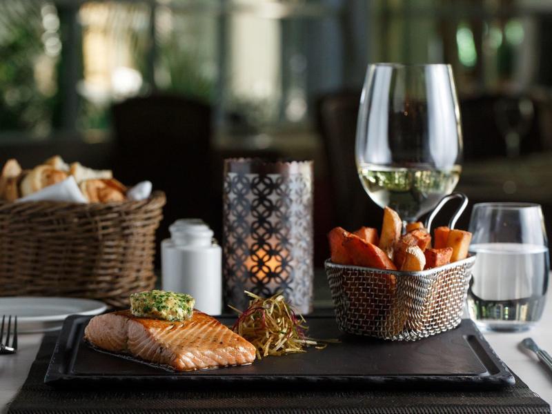 Tavola con pesce grigliato, cestini di pane e patatine, bicchieri di vino e acqua, candela in portacandele di vetro.