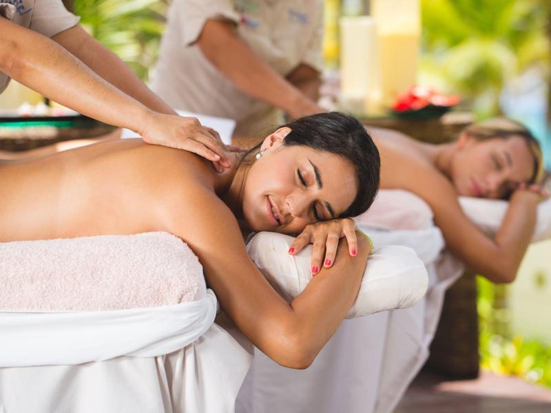 Due donne ricevono massaggi rilassanti alle spalle all'aperto su lettini da massaggio bianchi.