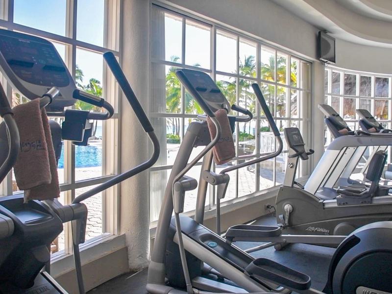 Fila di macchine cardio vicino a grandi finestre in una palestra luminosa con vista esterna.