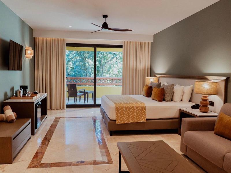 Camera d'hotel moderna con letto, divano, TV e balcone con vista sul verde.