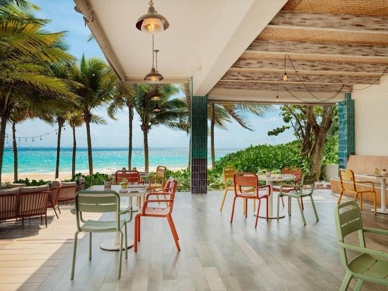 Caffè all'aperto sulla spiaggia con sedie colorate e palme vicino all'oceano.