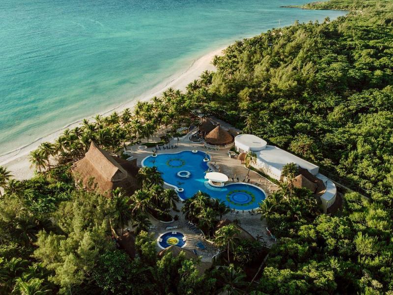 Un resort tropical isolato con piscine blu circondate da una rigogliosa foresta verde vicino alla riva dell'oceano.
