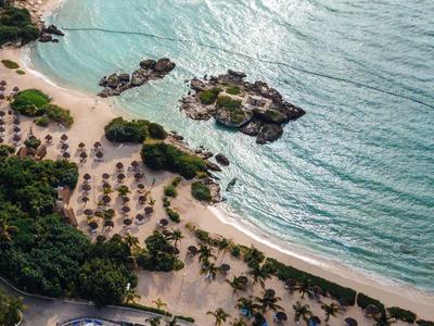 Veduta aerea di una spiaggia con palme, ombrelloni e acqua limpida e blu.