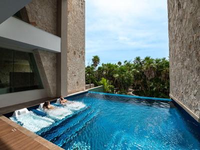 Piscina interna con sdraio in acqua e vista sulle palme in un hotel moderno.