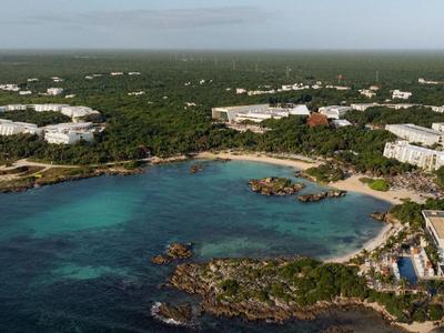 Vue aérienne d'une station balnéaire avec des hôtels entourés de forêt verte et d'eau claire.