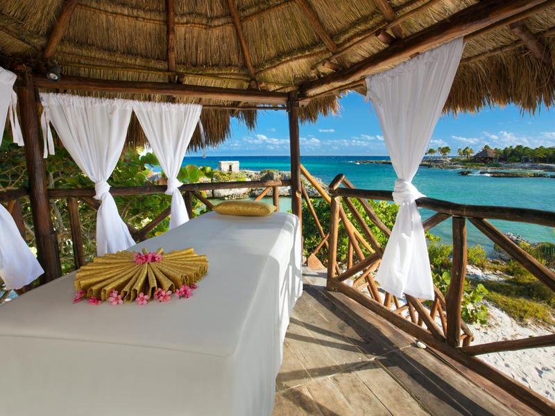 Lettino da massaggio sotto un tetto di paglia con vista mare e tende bianche.