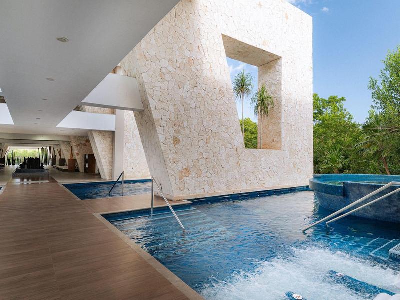 Piscina esterna moderna con cascata e vista sugli alberi accanto a un edificio dell'hotel luminoso.