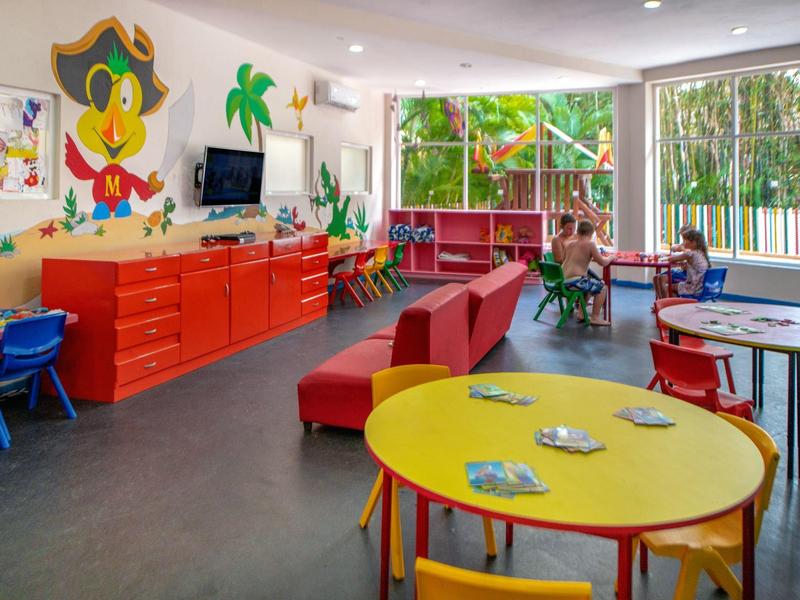 Bright children’s playroom with colorful tables, chairs, red storage cabinets, and wall decorations.