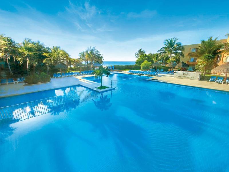 Open-air reception desk with blue zigzag tiles, a thatched roof, and hanging plants in a tropical setting.