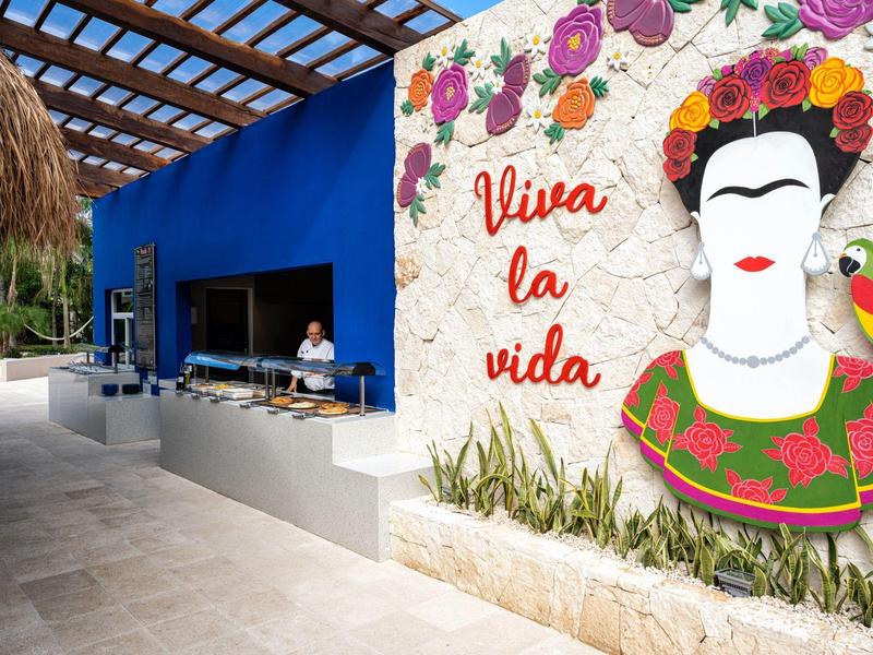 Outdoor bar area with a colorful mural saying 'Viva la vida' and tropical decor.