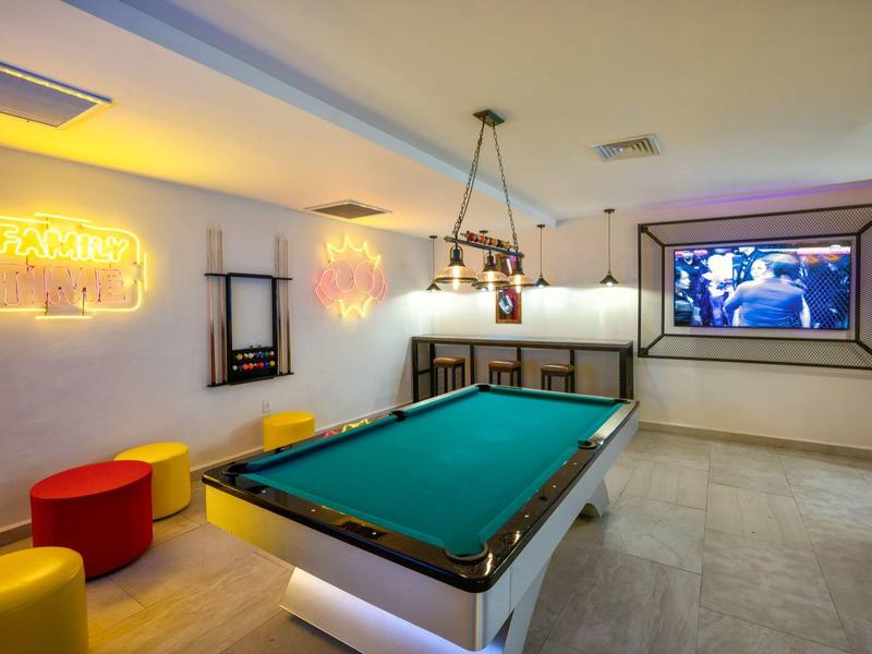 Indoor game room with a pool table, colorful stools, neon sign, and a large TV screen.