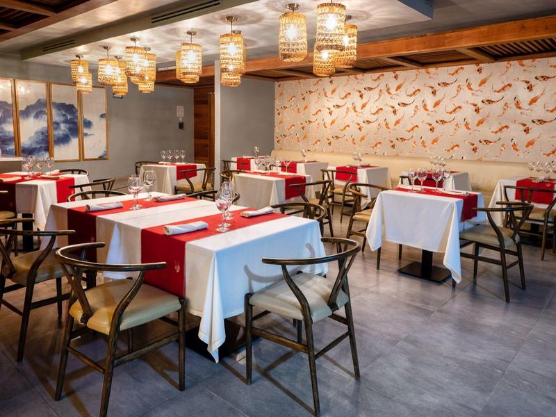 Elegant restaurant with white and red tablecloths, modern wooden chairs, and pendant lighting.