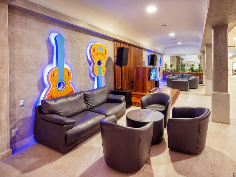 Modern hotel lounge with black leather sofa, chairs, guitar wall art, and warm lighting.