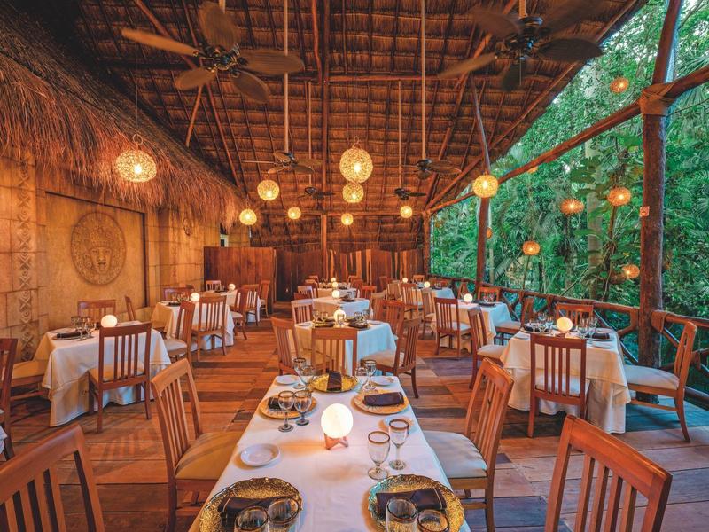 Cozy open-air restaurant with wooden furniture and warm hanging lights overlooking lush greenery.